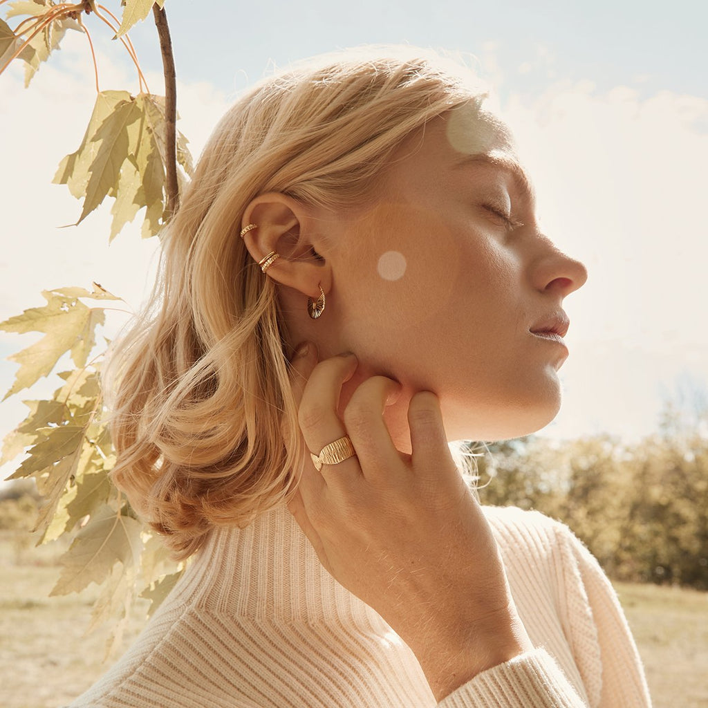 A young blonde lady, outside in nature, is wearing many gold jewelry pieces handmade in Montreal by local jewelry brand Véronique Roy JWLS. Find them all at jewellery store Ruby Mardi, in Little Italy.