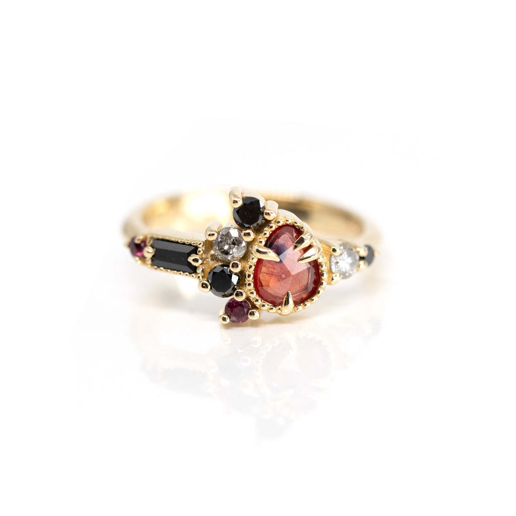 An artistic yellow gold fine ring featuring amorphous red rose cut sapphire, black diamonds, salt & pepper diamonds, ruby and black spinel, set in 10k yellow gold and photographed on a white background.