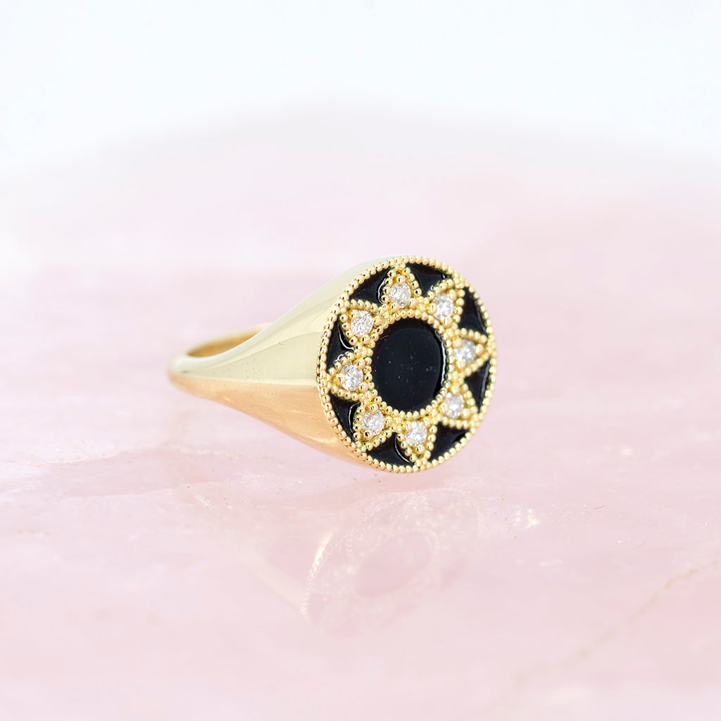 Side view of a yellow gold signet ring with black enamel and natural diamonds photographed on a rose quartz background. This fine jewelry piece was handcrafted in Toronto by independent jewelry designer Emily Gill and available exclusively at the best jewelry store in Montreal AND Canada, Ruby Mardi.