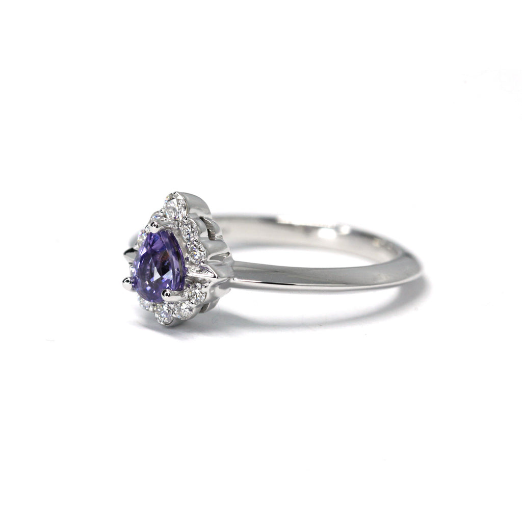 Pear Shape Purple Sapphire Engagement ring with a diamond halo on a white background by Ruby Mardi, a fine jewelry gallery in Montreal Little Italy, close by Bijouterie Italienne, and Rosemont, Outremont, Villeray, Parc Extension, Mile End, Mile Ex districts. White gold gemstone ring, bridal jewelry, wedding ring, ethical gem. Ruby Mardi offers custom jewelry services in Montreal. Lab grown diamonds, natural diamonds, Canadian diamonds, ethical diamonds, ethical gemstones.