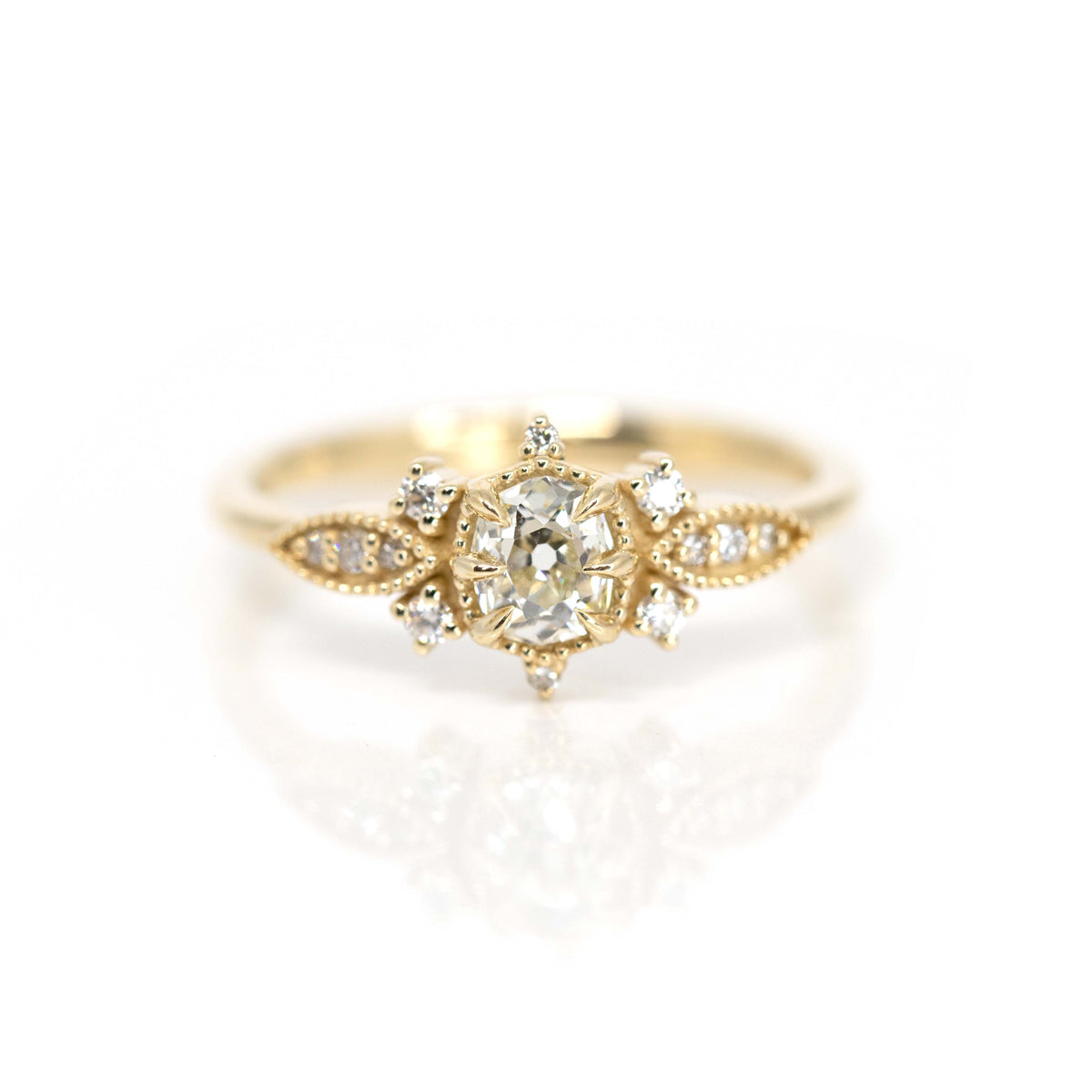 A beautiful engagement ring in solid  yellow gold with 13 natural diamonds. A work of art handmade by Nadia Werchola in Toronto, and exclusively available at Ruby Mardi in Montreal. The ring is seen on a white background. The central diamond is old-mine cut, and there are many multigrain details that gives a vintage vibe to the bridal jewel. 
