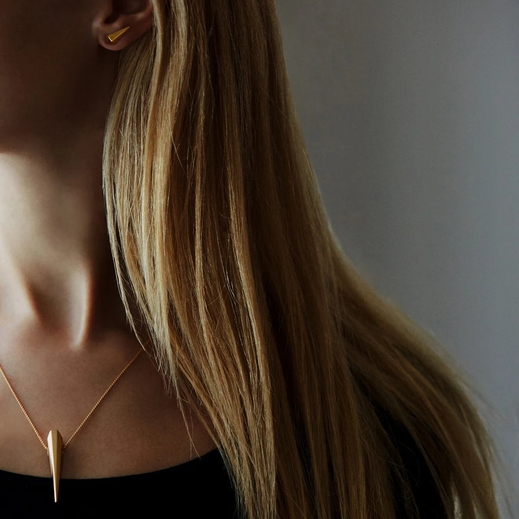 girl wearing vermeil gold edgy earrings and matching pendant mad in montreal by bena jewelry for the jewelry boutique ruby mardi on a dark background