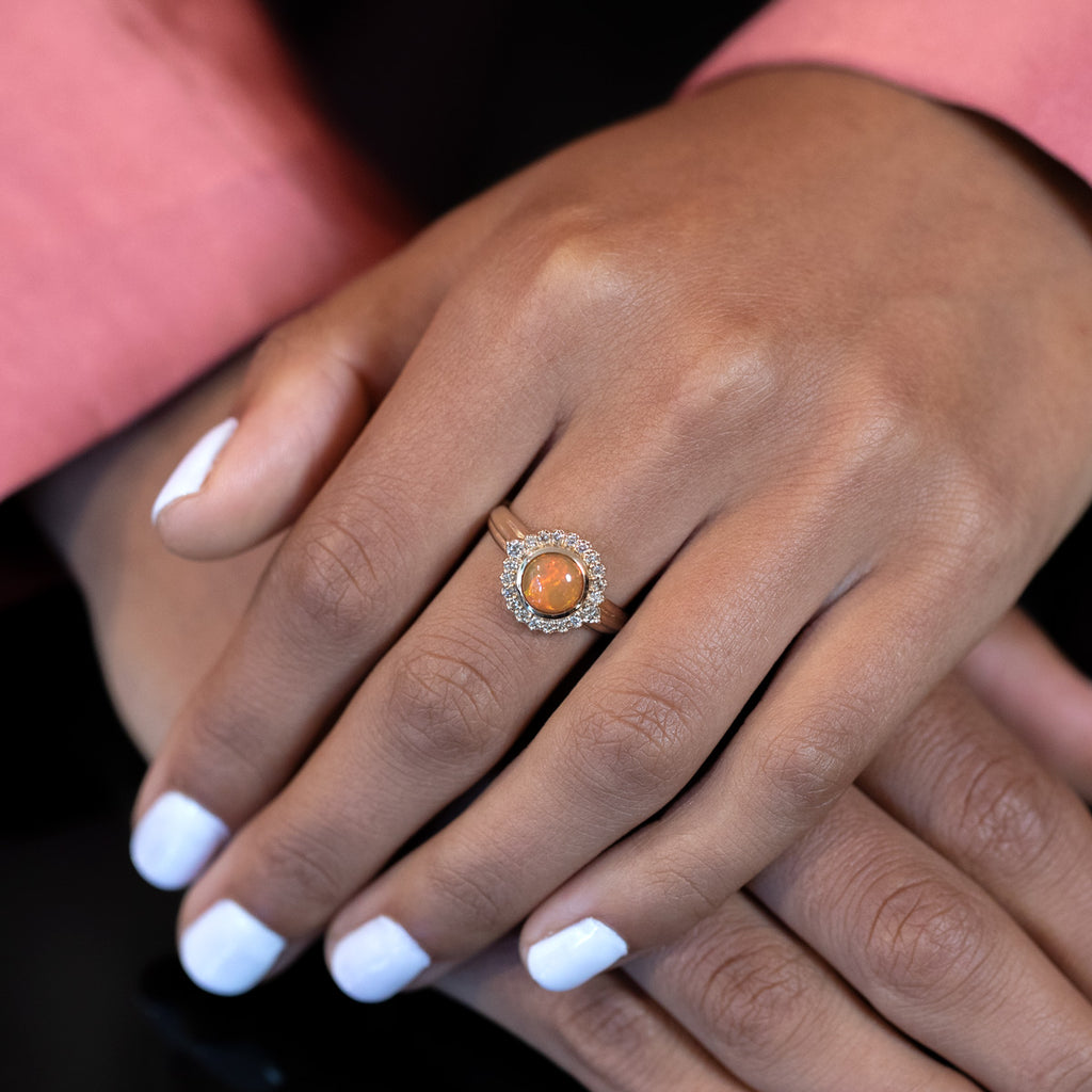 Product photo of the amazing ELENA: a yellow gold ring with a cognac diamond halo and a central orange opal by designer Bena Jewelry. Modern designer jewelry available at Ruby Mardi, the only fine jewelry gallery in Montreal. Custom jewelry services also offered.