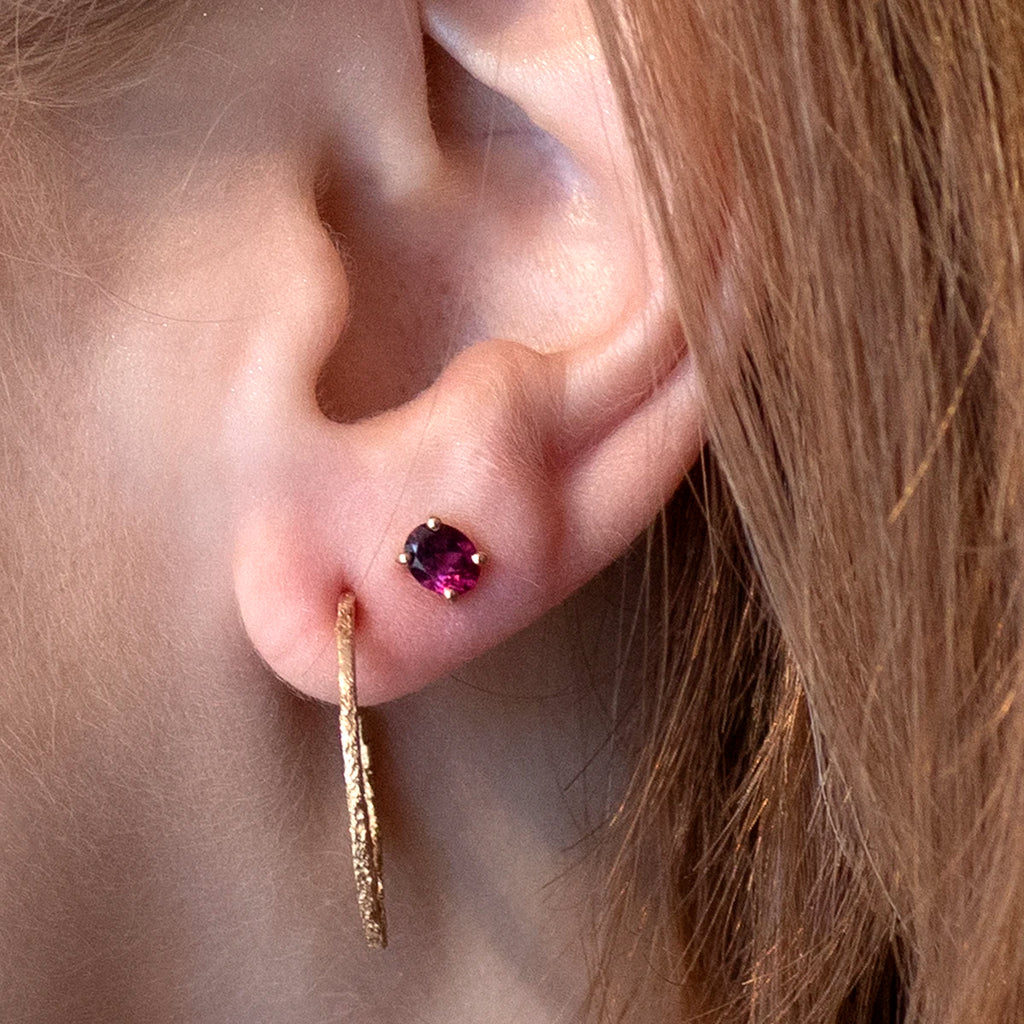 girl wearing two earrings a small oval shape garnet studs and desginer earrings yellow gold sand cast fine jewellery boutique ruby mardi montreal little italy jeweller