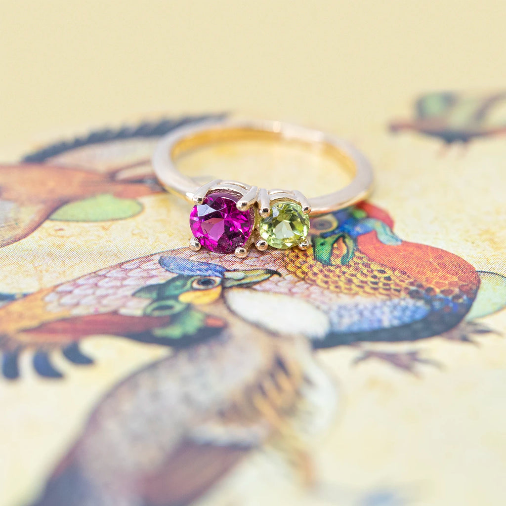 top view of toi et moi colored gemstone bridal ring with purple rhodolite garnet and peridot gems gold ring on a multi color background