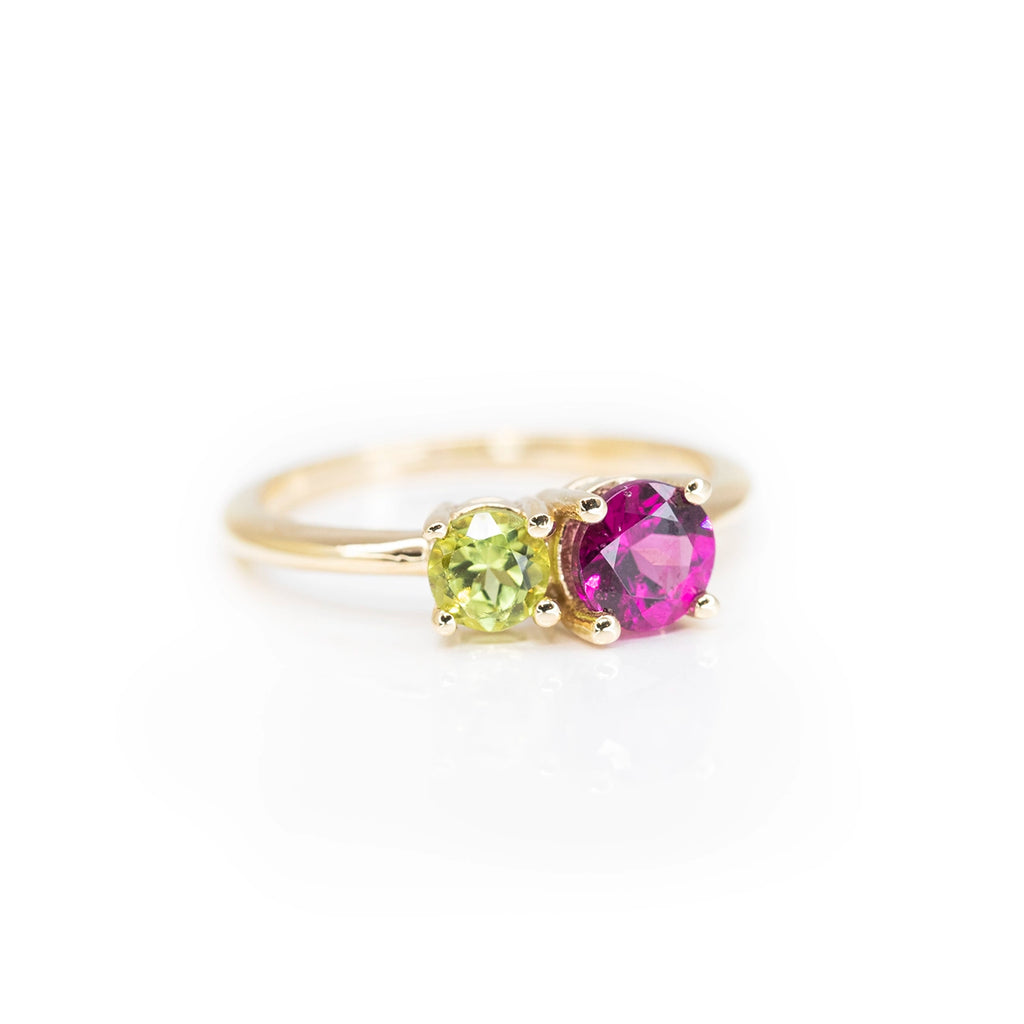 side view of yellow gold minimalist colored gemstone ring with purple rholdolite garnet peridot toi et moi engagement ring made in montreal on a pink background