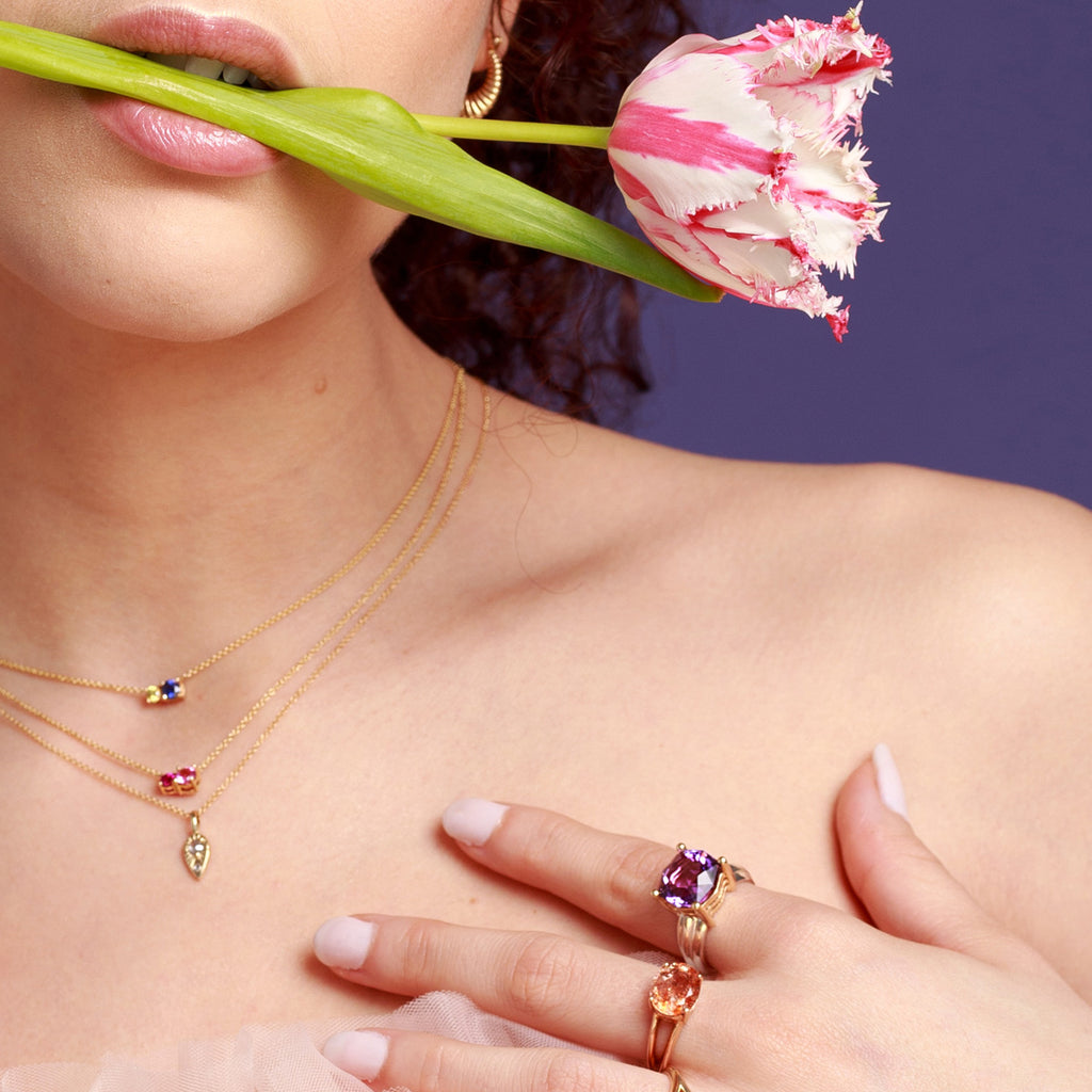 Young lady in close up wearing many statement gemstones rings and delicate gemstone pendants featuring sapphire, tourmaline, diamond, amethyst and smoky quartz.