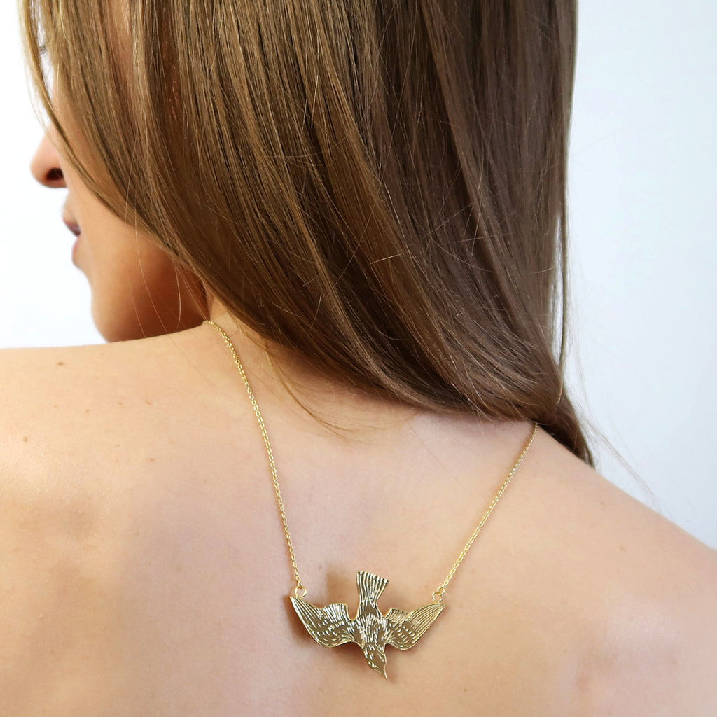 Beautiful and quite big gold vermeil flying bird pendant, handmade in Toronto by jewelry brand Invidiosa Jewelry, seen worn by a red head lady. This original and funky necklace is available in Montreal, only at Ruby Mardi.