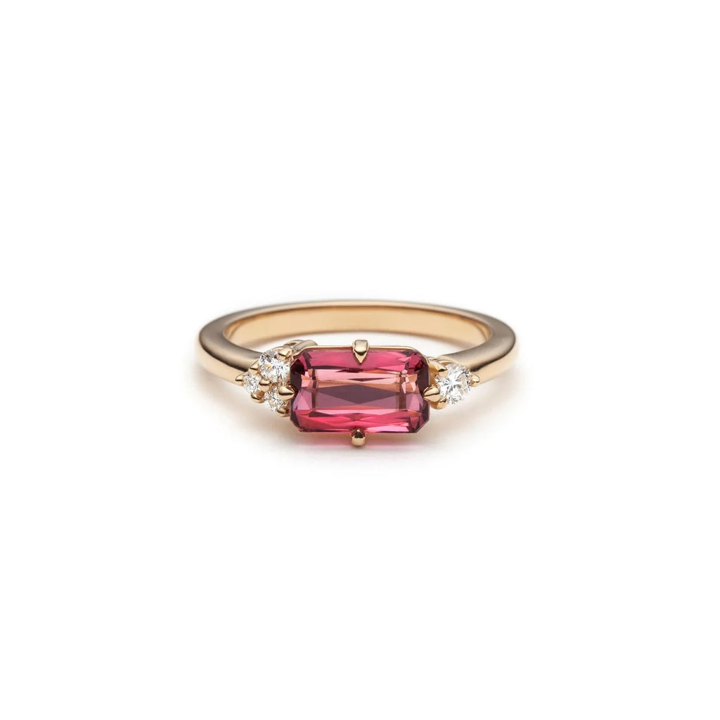 An alternative engagement ring photographed on a white background. The ring features a central peachy/pink spinel and side round brilliant diamonds that are set asymmetrically for a totally unique look!
