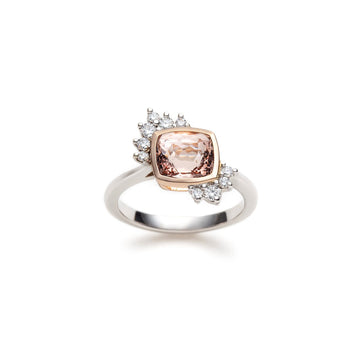 An engagement ring in white gold and rose gold with a cushion morganite and round brilliant diamond accents is seen photographed on a white background. This one-of-a-kind feminine asymmetrical wedding ring was handmade in Montreal by independant jewellery designer Justine Quintal. This piece of fine jewelry is only available at Ruby Mardi, the most original and unique jewelry store in Montreal.
