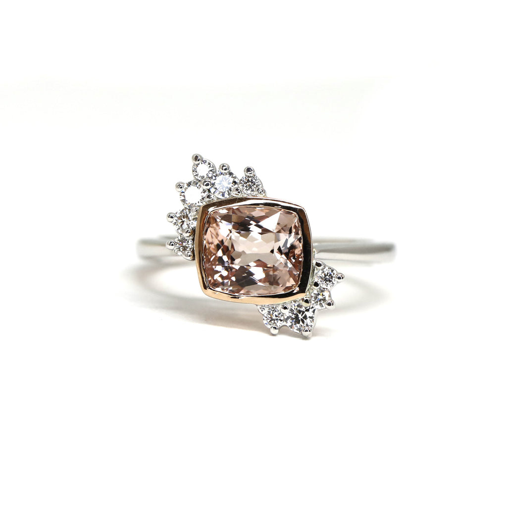 Front view of an engagement ring in white gold and rose gold with a cushion morganite and round brilliant diamond accents seen on a white background. This one-of-a-kind feminine asymmetrical wedding ring was handmade in Montreal by independent jewellery designer Justine Quintal. This piece of fine jewelry is only available at Ruby Mardi, the best jewelry store in Montreal.