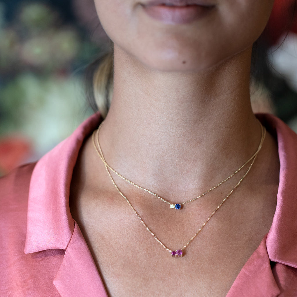 A young woman is wearing two gemstone gold pendants featuring sapphire, tourmaline and rubelite. Designer jewellery handmade in Montreal by Lico Jewelry and available at Ruby Mardi concept store that also offers flowers, custom made jewelry and engagement rings.