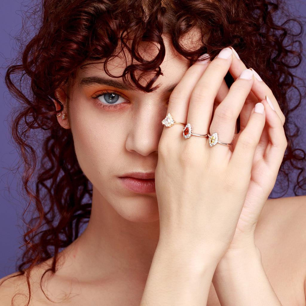Diamond halo engagement rings worn by a bare-shouldered young woman against a purple background. These wedding rings were made by Ruby Mardi, a high-end fine jewelry store located in Montreal's Little Italy. Natural and laboratory diamonds. Canadian diamonds. Custom jewelry design in Montreal.