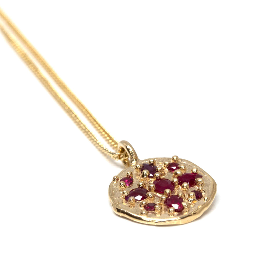 An organic handmade gold pendant medaillion with gold granules and encapsulated rubies seen on a white background. Find this beautiful piece of fine jewelry by Meg Lizabet at Ruby Mardi, a high end jewelry store located in Montreal's Little Italy.