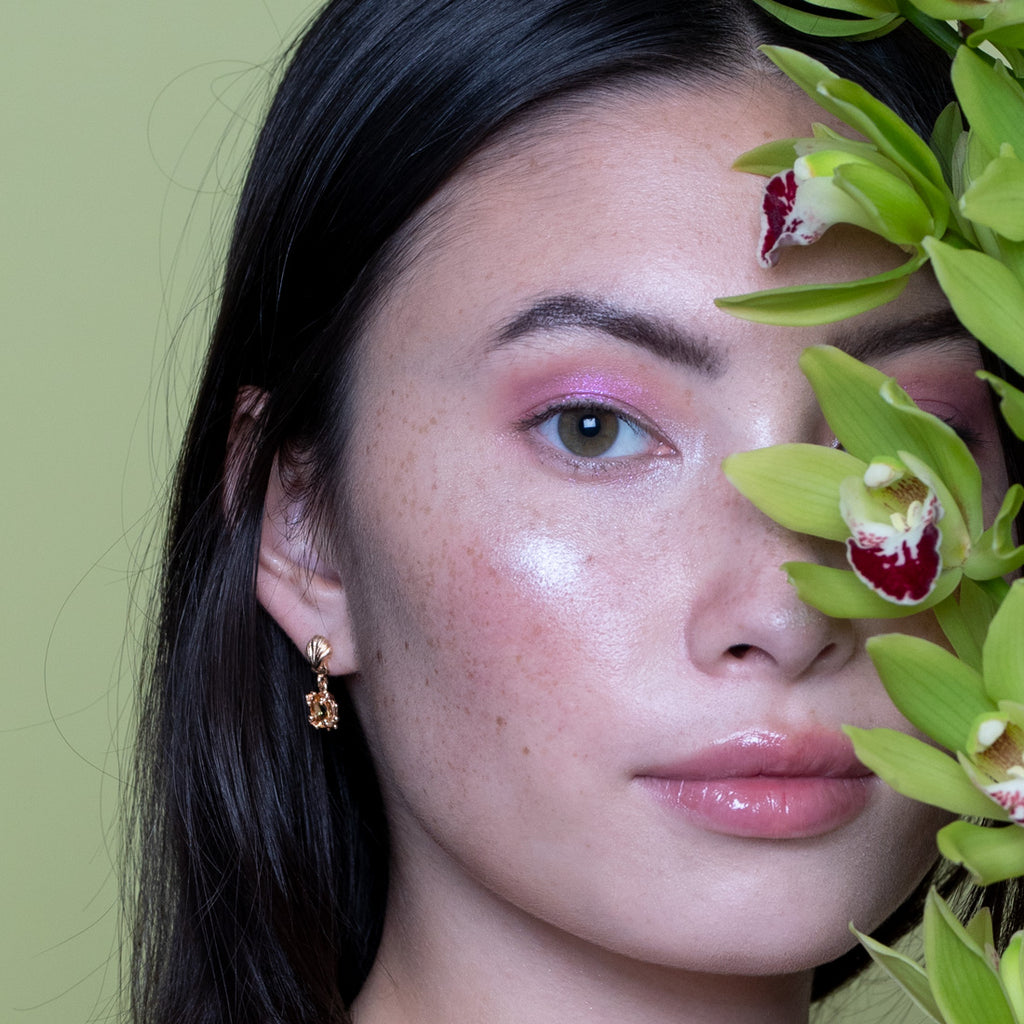 girl wearing meg lizabeth yellow gold sapphire earrings on a green background and holding a flower