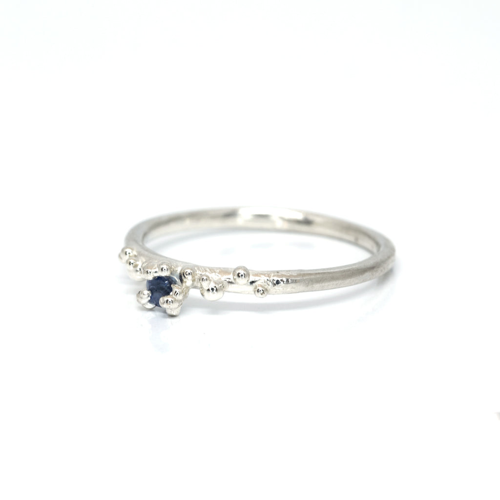 Organic ring by Meg Lizabet made of sterling silver and featuring a small blue sapphire and silver granules. 