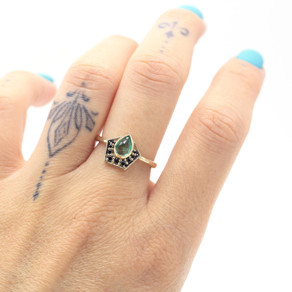 Nefertiti engagement ring or right hand ring worn by a hand with tattoes and turquoise nails. A stunning ring with an exotic vibe featuring emerald, black diamonds and salt and pepper diamonds. 