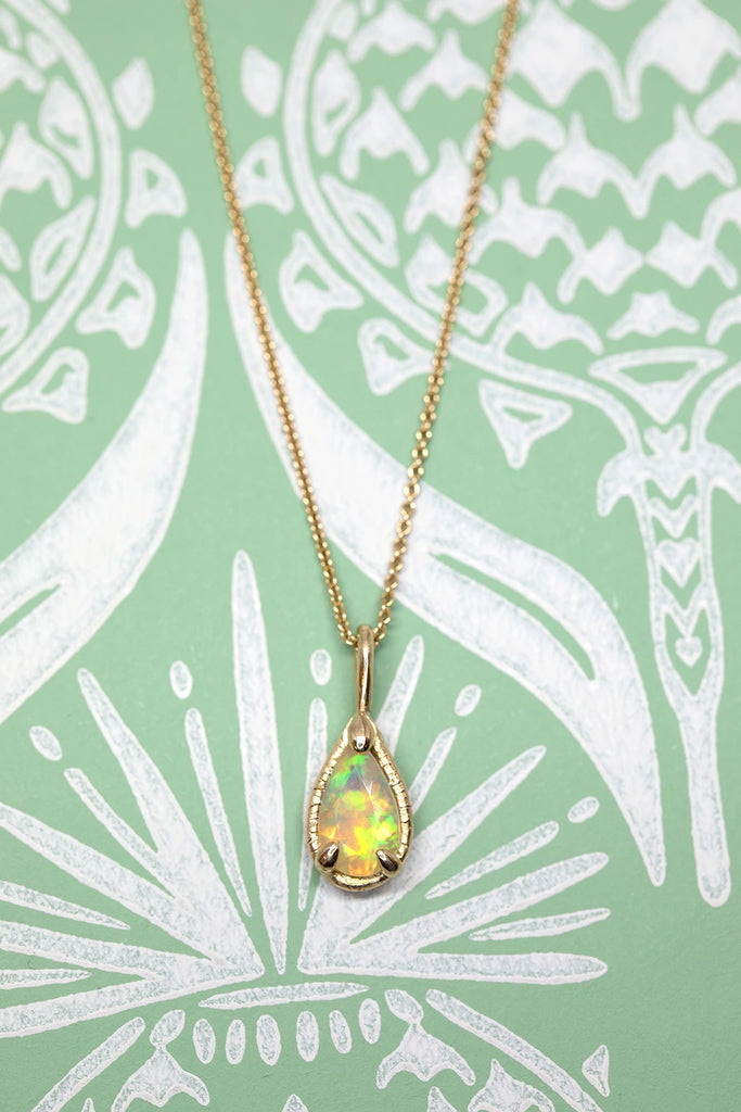 front view of pear shape opal yellow gold pendant made in montreal by artisan designer sheena for the jeweler ruby mardi on green and white background