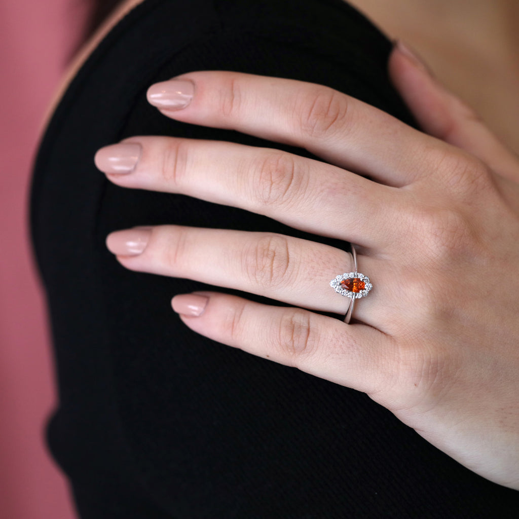 A lady wear a white gold engagement ring with a diamond halo and a beautiful central orange gemstone (a spessartite garnet). Find more bridal jewelry in Montreal at Ruby Mardi, the only fine jewelry gallery in town.