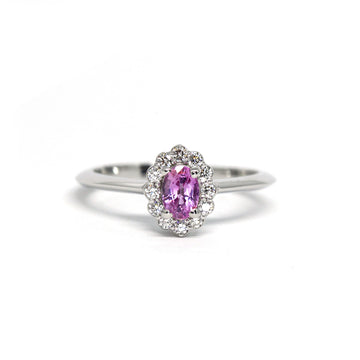 Beautiful engagement ring with a romantic and vintage look photographed on a white background. The white gold ring features an oval pink sapphire with a diamond halo. It’s available online or in Montreal at fine jewelry store Ruby Mardi. 