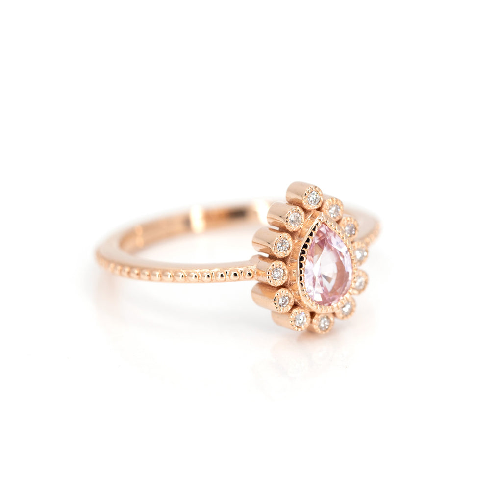 Side view of the splendid ring of the jewelry designer Emily Gill, made in pink gold with a magnificent natural sapphire of light pink color and surrounded by a delicate diamond halo. The ring is handmade with a milligrain. This unique piece of jewelry is made in Canada and is available at Ruby Mardi Bridal Jewelry.