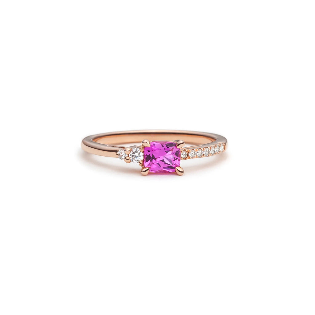 A classic engagement ring, but with a twist! The jewelry designer Justine Quintal used rose gold, and chose a beautiful bright pink sapphire as the central stone. The band shows round brilliant diamonds, as accents on a side, and as a pavé on the other, for an unusual asymmetrical look that ends to be really elegant. The jewellery piece is seen on a white background.