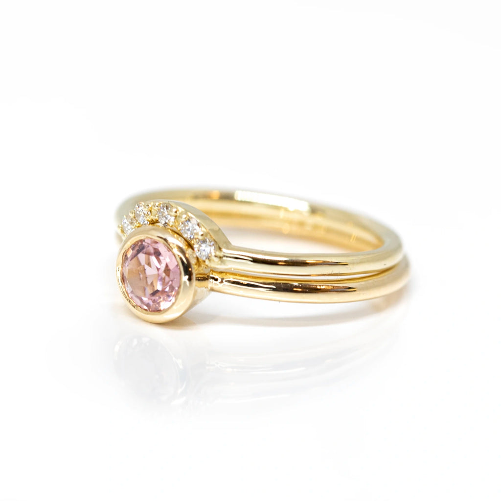 side view of diamond band and matching pink tourmaline bezel setting engagement ring made in montreal by the jewelry designer sheena for the jeweler boutique ruby mardi in montreal little italy on pink background