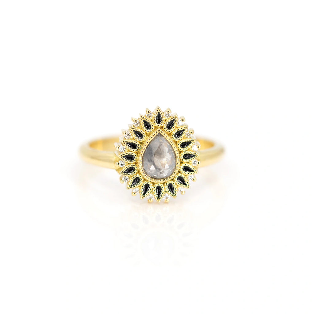 An 18-carat yellow gold ring is photographed from the front against a white background.  This is a unique designer ring featuring a pear-shaped salt-and-pepper diamond at its center, surrounded by several small black pear shapes in enamel. Completing the composition are 16 natural diamond accents. This alternative engagement ring is available only at Ruby Mardi.
