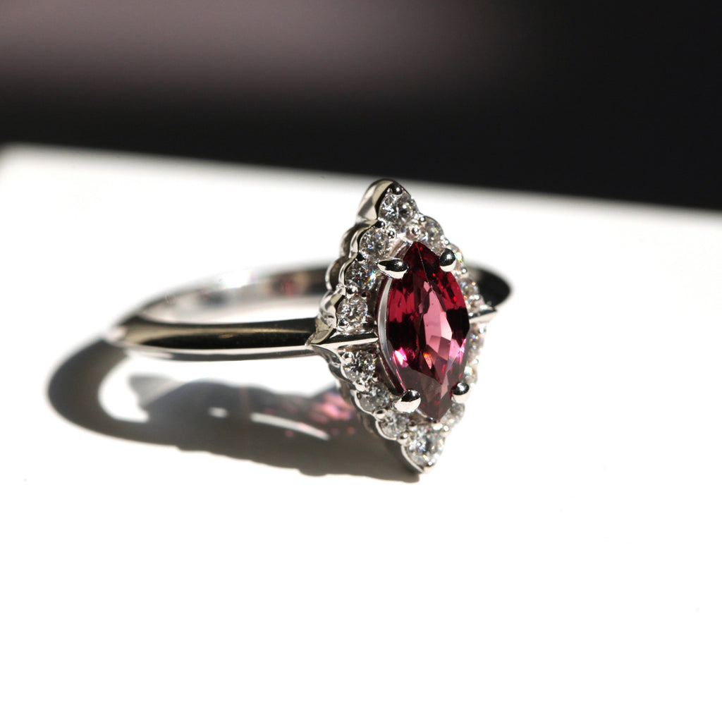 A red garnet with a halo of diamonds engagement ring seen in the shadows. White gold and red gemstone, a beautiful and meaningful ring. 