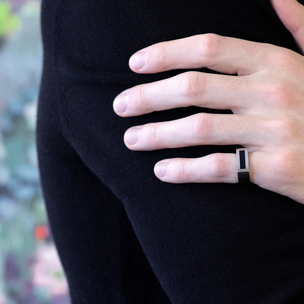men wearing a pinky white gold ring with a black onyx strip with a black shirt on a multi color background