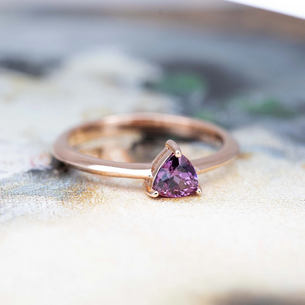 side view of custom made trillion shape colored gemstone purple rhodolite garnet rose gold engagement ring on multi color background