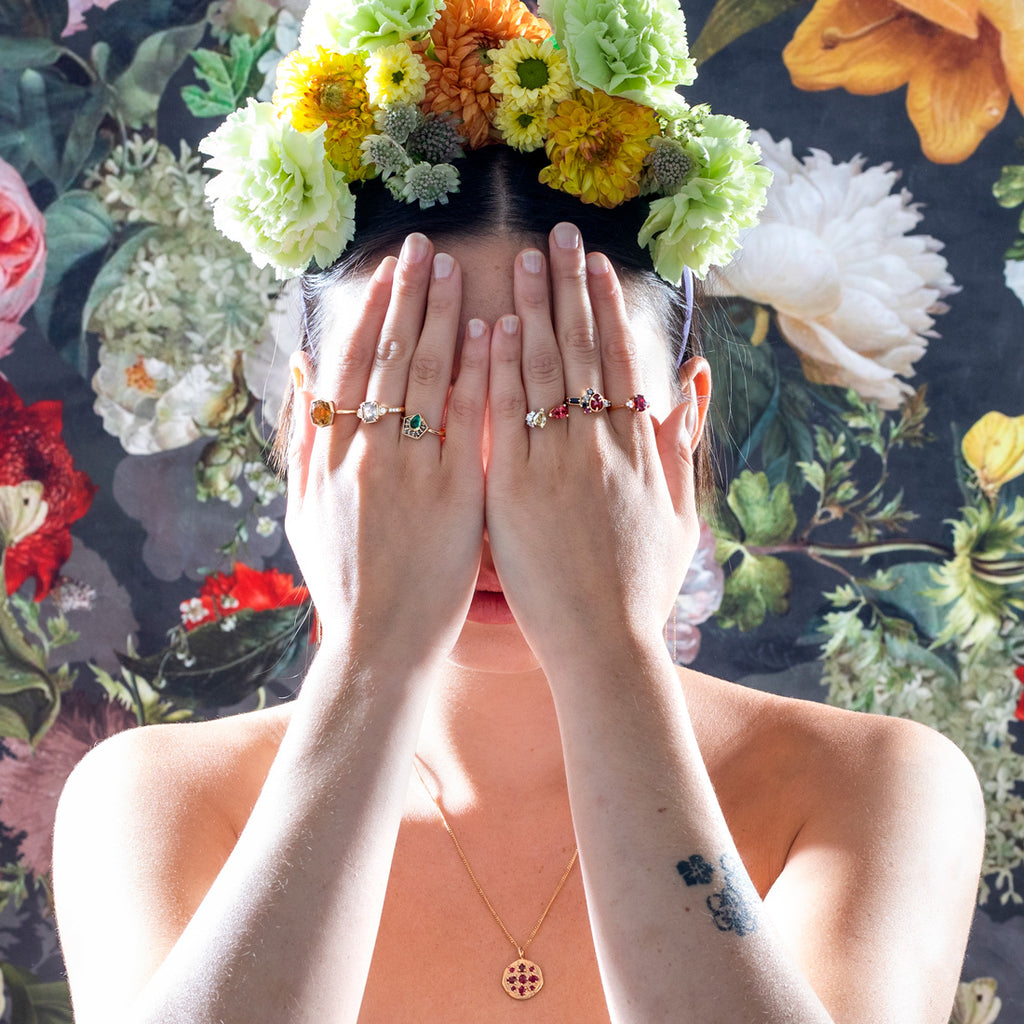 A lady with a flower crown à la Frida Khalo is hidding her face with her two hands, so we see the 6 gemstone rings she wears. Citrine, diamond, emerald, spinel, ruby, sapphire and garnet. Alternative engagement rings by Canadian jewelry designers.