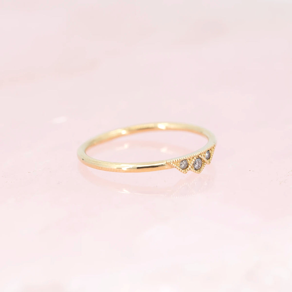 A delicate salt & pepper gold ring with milgrain detailing and geometric shapes photographed over natural rose quartz and seen from the side. An alternative bridal jewelry piece or right hand ring that can be found at fine jewellery store Ruby Mardi in Montreal.
