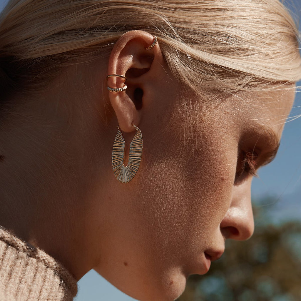 A young blonde lady photographed outside is wearing a big textured gold vermeil hoop, as well as three delicate ear cuffs, also in gold plated. Handmade in Montreal by Véronique Roy JWLS, and available at Ruby Mardi.