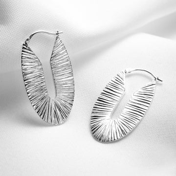 Large and chunky oval textured sterling silver hoops handmade in Montreal by Veronique Roy JWLS photographed on a white fabric. Available at jewelry store Ruby Mardi, in Little Italy. 