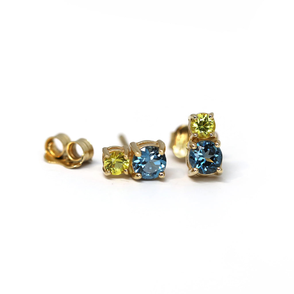 Gold gemstone stud earrings featuring yellow sapphire and Swiss Blue Topaze. Jewelry available at fine jewellery store gallery Ruby Mardi, located in Montreal’s Little Italy. 
