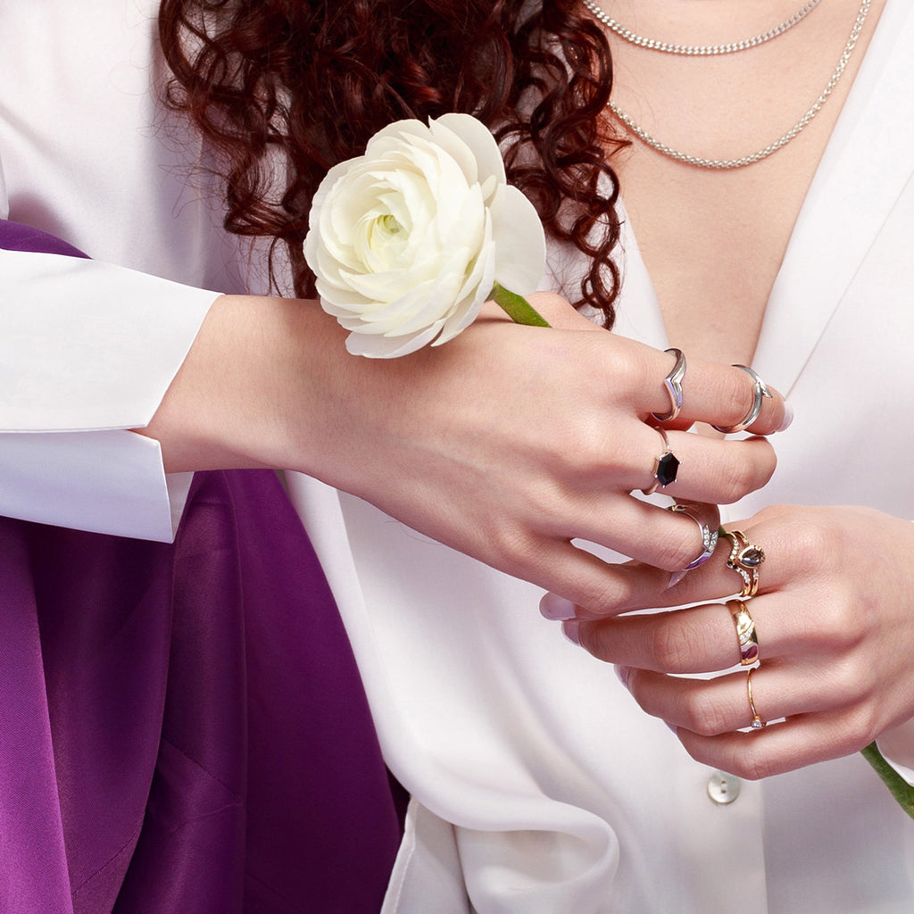 A lady in close up wearing many rings from different Canadian jewelry designers. Gold rings, diamond rings, wedding bands, silver rings, black spinel ring. She’s also wearing three silver chains. 