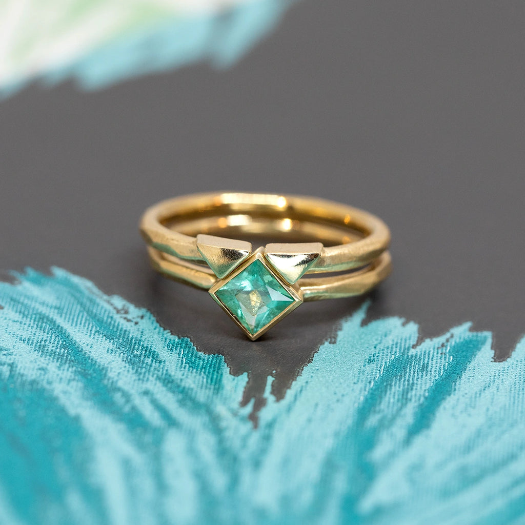 princess cut emerald yellow gold engagement ring with it's matching made in montreal by the artisan jewellery designer sheena for the jeweler ruby mardi on green blue and black background