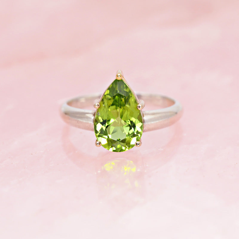 Photography on rose quartz of a beautiful ring in 14k yellow gold and sterling silver featuring a huge natural green gem, peridot, by designer Bena Jewelry. Find the most exquisite designer jewelry at Ruby Mardi, a fine jewelry store in Montreal that presents the work of the most talented Canadian jewelry designers. Custom jewelry services also offered.