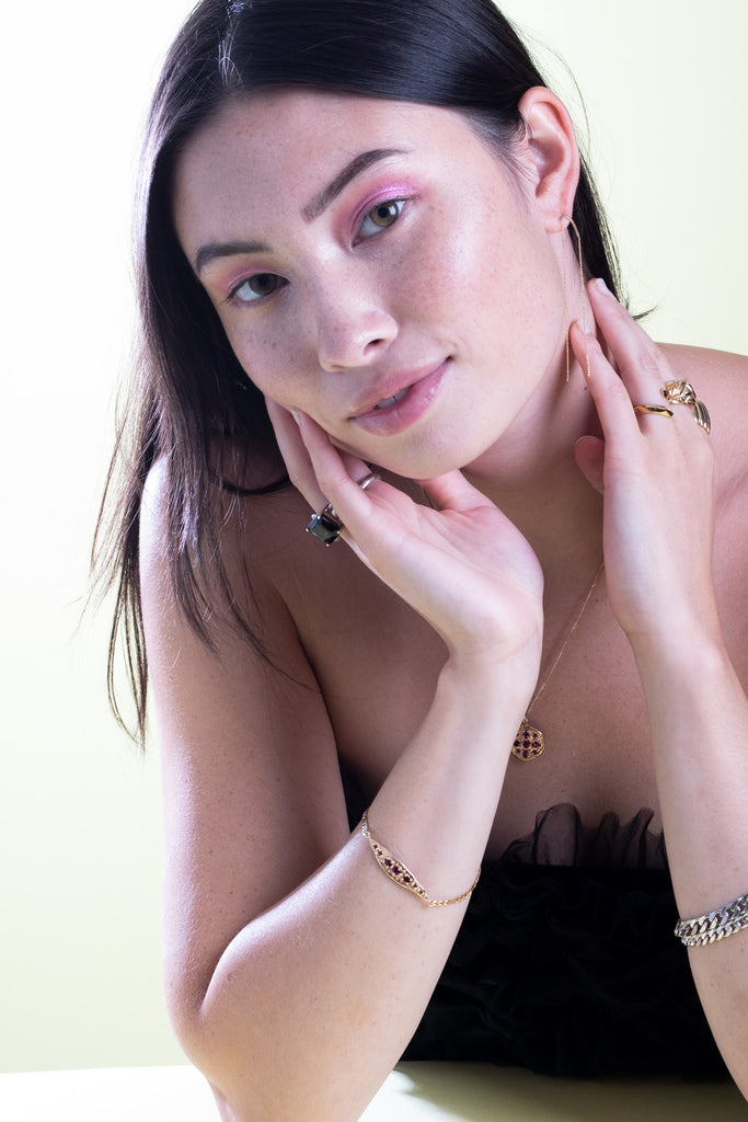 A young lady is wearing multiple pieces of jewelry handmade in Canada and available at jewelry store Ruby Mardi in Montreal : ruby pendant, ruby bracelet, silver curb chains, 18k yellow gold pendant earrings, gold vermeil statement rings and a huge smoky quartz silver ring.