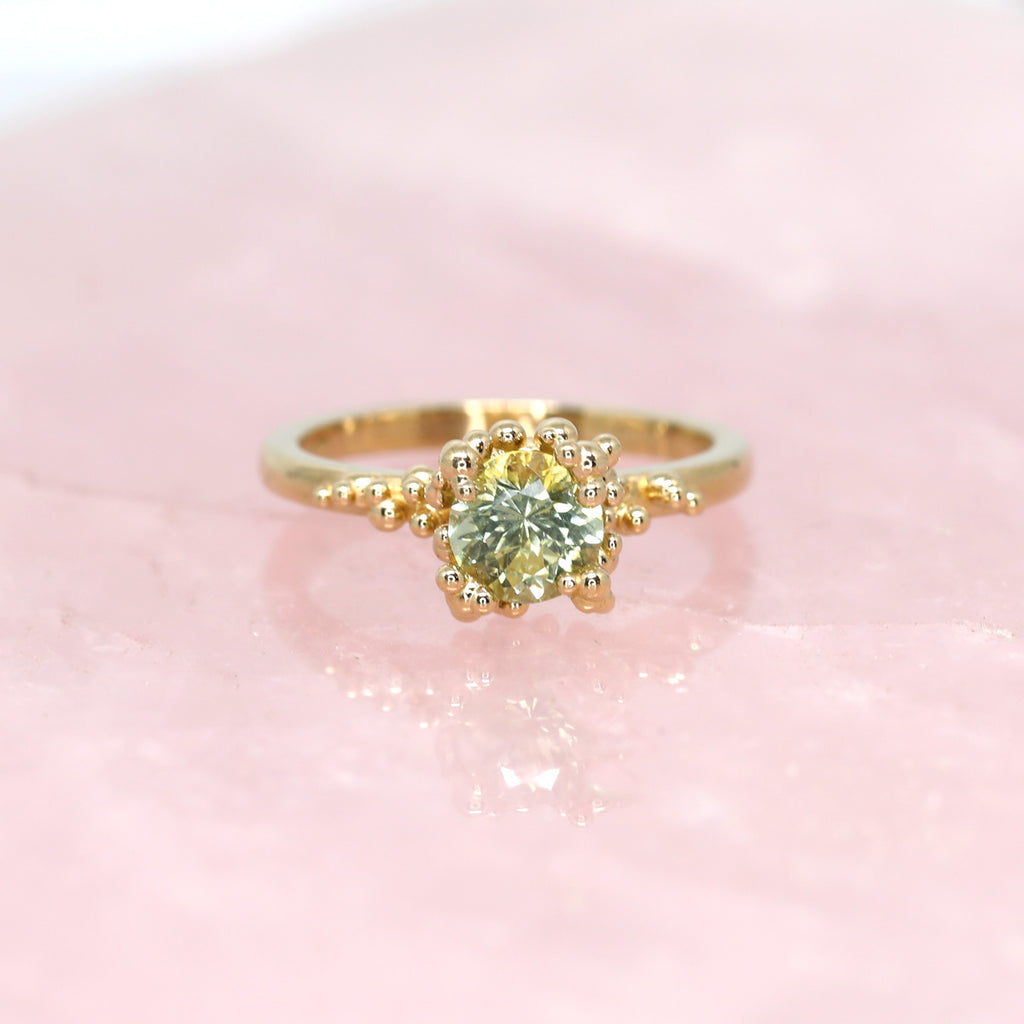 Stunning engagement ring by Meg Lizabet Jewellery photographed on pink quartz. A yellow gold organic ring with gold granules and encapsulated bicolor sapphire (yellow & green) of 1.08ct. One of a kind ring available high end jewelry store Ruby Mardi in Montreal.