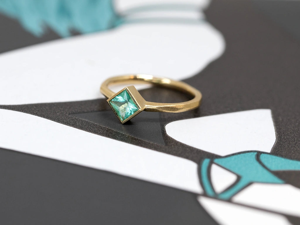single princess cut emerald gold bezel setting edgy engagement ring made by artisan sheena montreal jeweler boutique ruby mardi on dark background