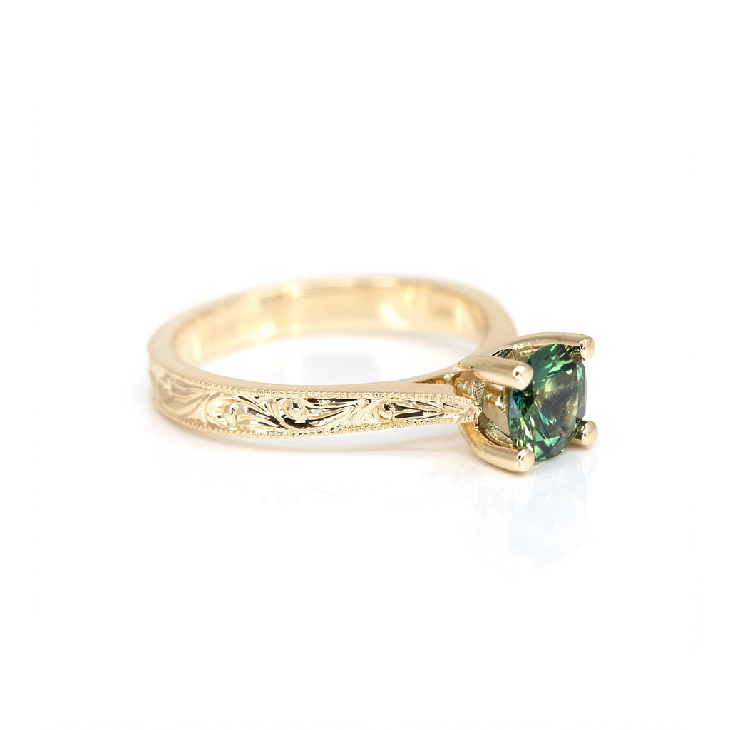 yellow gold engraved engagement ring made by hand greenish blue australian sapphire fine jewelry designed by Deborah Lavery at the boutique ruby mardi in montreal on a white background