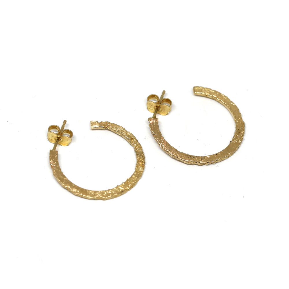 Product photography of Sand cast open hoops in 14k yellow gold by Canadian jewelry designer Meg Lizabet, seen in close up. These earrings are available at Ruby Mardi, the only fine jewelry gallery in Montreal.