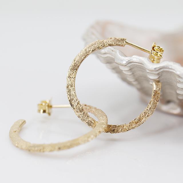 Beauty shot of Sand cast open hoops in 14k yellow gold by Canadian jewelry designer Meg Lizabet, seen in close up. These earrings are available at Ruby Mardi, the only high end jewelry gallery in Montreal.