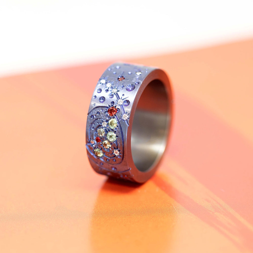 top view of a colored gemstones men ring in titanium purple color and ruby and sapphire gems best jewelry designer in montreal Janine de Dorigny works with boutique ruby mardi to offer the finest bridal design on orange background