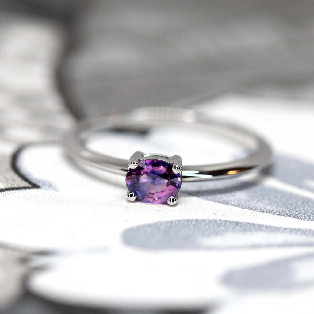 A magical two colours sapphire with pink and purple hues, set in 14k white gold and photographed on a wallpaper. Beautiful, simple and elegant solitaire engagement ring.