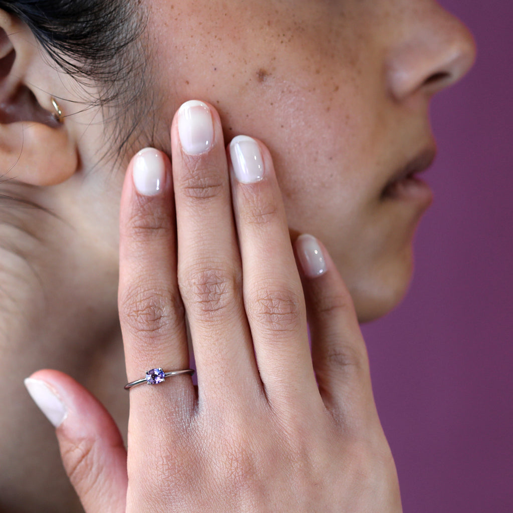 A young lady wears a delicate simple white gold ring with a beautiful bicolour purple sapphire. Find more fine jewelry at our store in Montreal’s Little Italy.