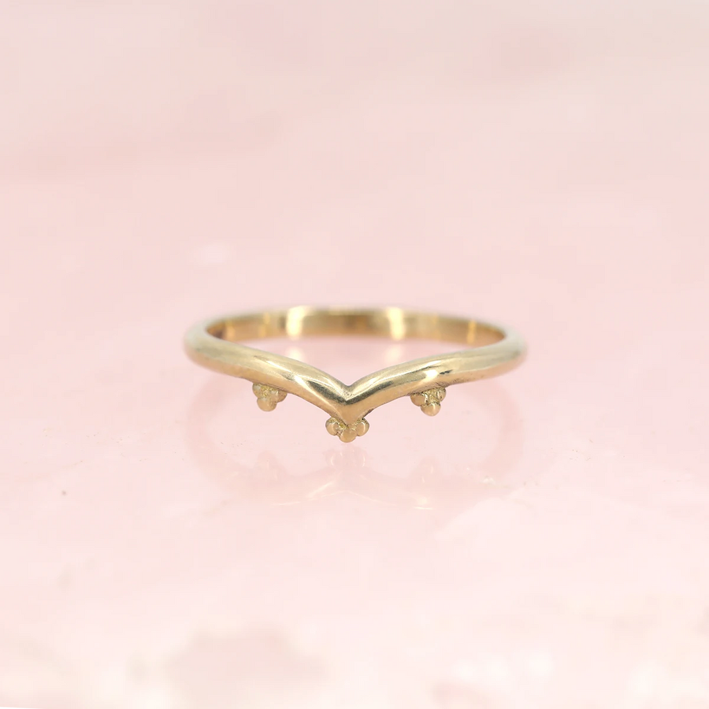 Yellow gold band in V shape with chevron photographed on a quartz rose background. Alternative wedding jewelry that can be found at fine jewellery boutique Ruby Mardi in Montreal’s Little Italy.