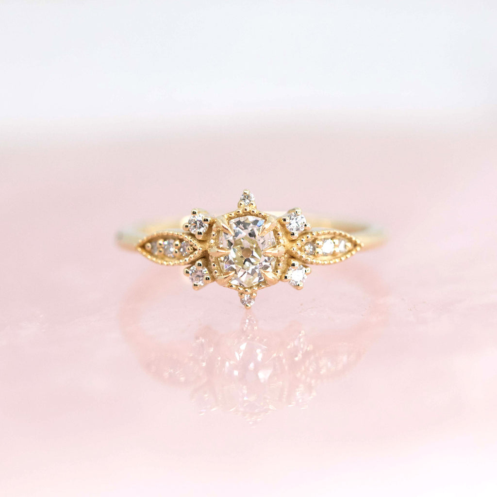 Beautiful engagement ring in 10k yellow gold with 13 natural diamonds photographed on a rose quartz background. Work of art handmade by Nadia Werchola in Toronto, and exclusively available at Ruby Mardi in Montreal.